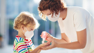Mother and child wearing facemasks and using hand sanitizer while out in public during COVID-19 pandemic.