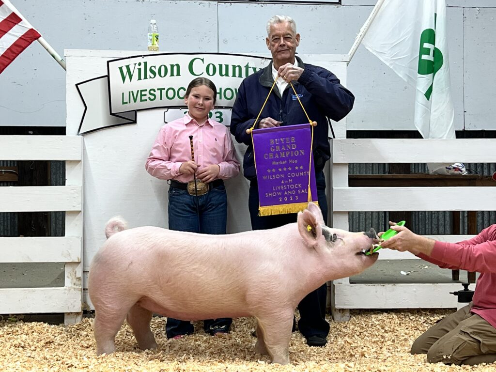 A child poses with a pig and a Buyer Grand Champion banner.
